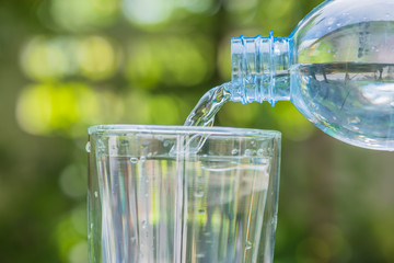 plastic bottle pouring water into a glass on green blurry backgr