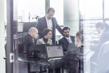 Wall Mural - Workplace in modern office with business people brainstorming viewed trough the glass door with reflections in it. Businessmen working on laptop during the meeting.