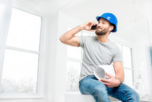 Handsome Repairman Or Builder In Helmet Talking With Phone With Drawings In The White Interior