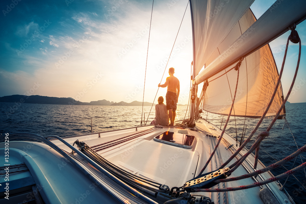 Couple enjoying sunset from the deck of the sailing boat moving in a sea - obrazy, fototapety, plakaty 