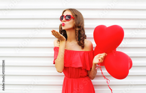 Portrait woman in red dress sends air kiss with balloon heart sh Poster