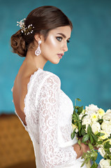 Fashion bride in vintage dress with no veil on a turquoise background with a bouquet of flowers in their hands