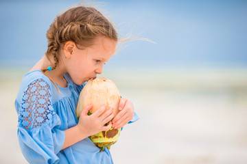 Little adorable girl drinking coconut milk on the beach