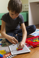 Wall Mural - Concentrated kid playing with toys construction tool kit while sitting on the floor in his room