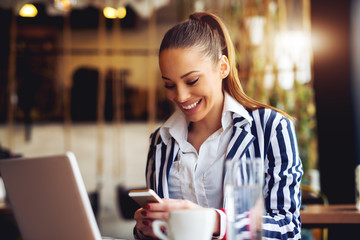 Young beautiful woman looking at smart phone at cafe bar.