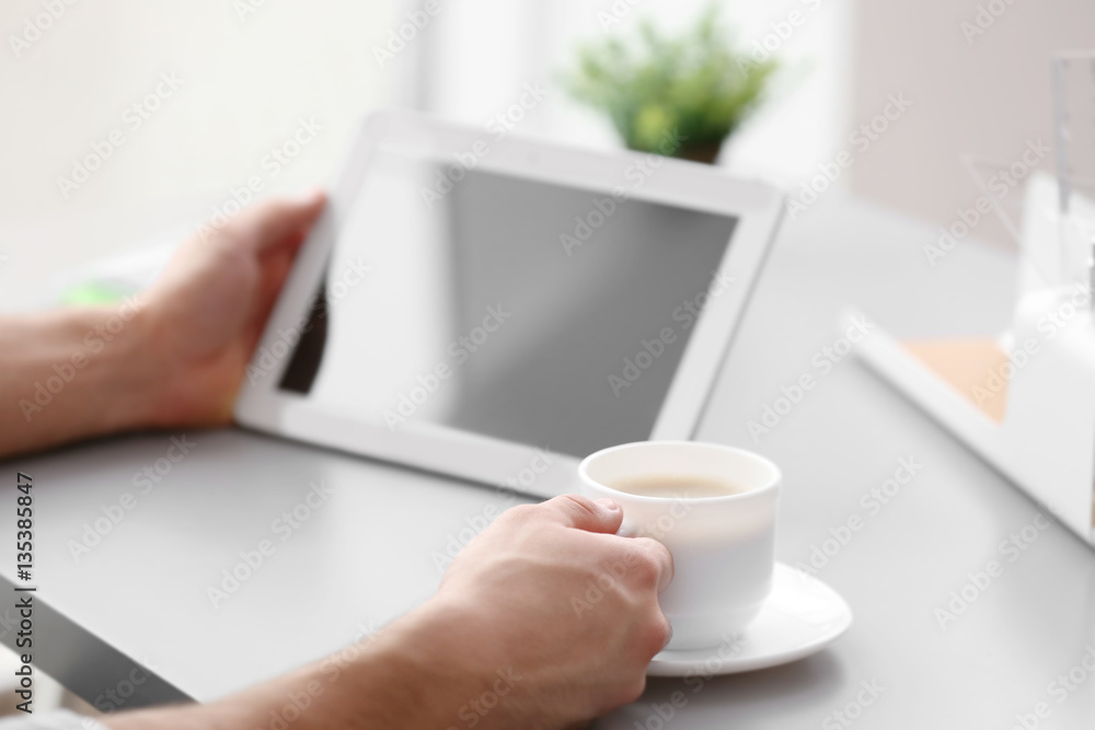 Handsome young man with tablet drinking coffee at home
