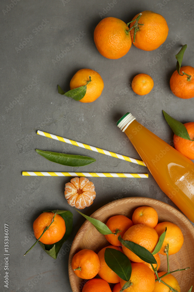 Tangerines and bottle of juice on grey background