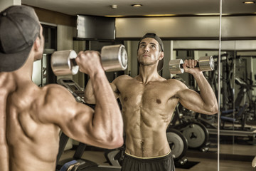 Wall Mural - Handsome shirtless muscular young man exercising shoulders in gym with dumbbells