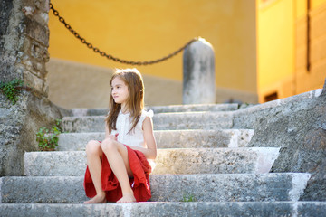 Adorable little girl sitting on the stairs on warm summer day in Gargnano town in Italy