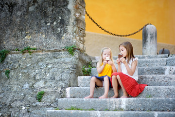 two cute little sisters eating ice-cream while sitting on the stairs on summer day