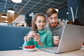 Man and woman drinking coffee and eating desert in a cafe. Two people, man and woman with laptop in cafe communicate, laughing and enjoying the time spending with each otherand. Couple in love on a