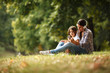 © BalanceFormCreative - Mother and daughter sitting on grass and listening to music on smart phone.