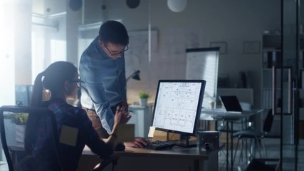  Late at Night in the Office, Male and Female Engineers Discuss  Blueprints Shown on Her Display. Office Looks Modern, with Blueprints on Walls.  Shot on RED Cinema Camera 4K (UHD).