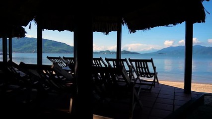 Wall Mural - Empty deck chairs on the roof of palm leaves. the tranquil turquoise sea, blue sky with few clouds.