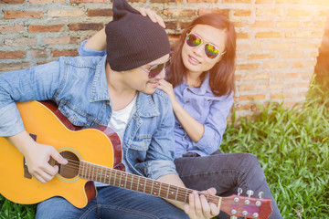 Poster - Hipster man playing guitar for his girlfriend outdoor against br