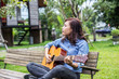 © chaunpis - Beautiful young woman playing guitar sitting on bench, Happy tim