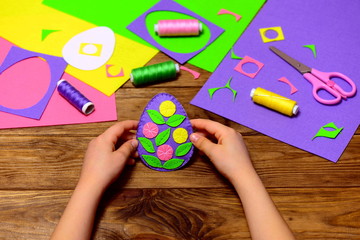 Wall Mural - Child holds a felt Easter egg ornament in his hands. Small child made easy Easter crafts. Sewing supplies on a wooden table. How to decorate a felt Easter egg with flowers and leaves