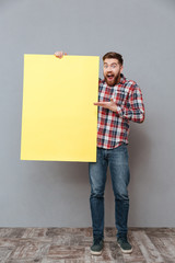 Wall Mural - Shocked bearded man holding copyspace board and pointing