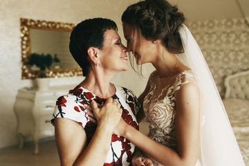 Happy mother holds bride's hand standing with her in the room