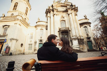 Young Man And Woman Sits On Bench Near Old Cathedral