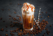 Cold coffee drink frappe (frappuccino), with whipped cream and caramel syrup, with straws and grains of coffee on a dark gray stone table, copy space