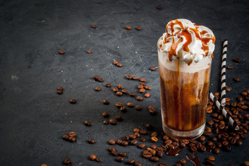 Cold coffee drink frappe (frappuccino), with whipped cream and caramel syrup, with straws and grains of coffee on a dark gray stone table, copy space