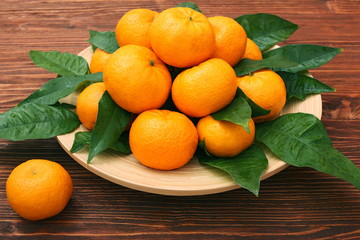 Wall Mural - Ripe orange tangerines with green leaves in plate