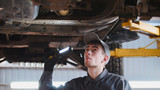 Fototapeta  - Mechanic with thr lamp is checking the bottom of car in garage automobile service, close up