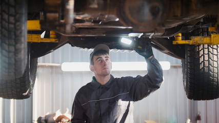 Mechanic with thr lamp is checking the bottom of car in garage automobile service, wide angle