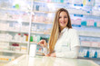 © Mediteraneo - Smiling attractive woman pharmacist displaying a box of tablets or a product in her hands as she stands behind the counter alongside shelves of stock