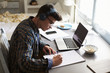 © Monkey Business - Teenage boy wearing headphones works at desk in his bedroom