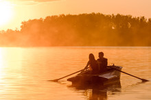 Love And Romantic Golden River Sunset. Silhouette Of Couple On Boat Backlit By Sunlight
