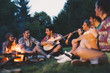 © NDABCREATIVITY - Happy friends playing music and enjoying bonfire