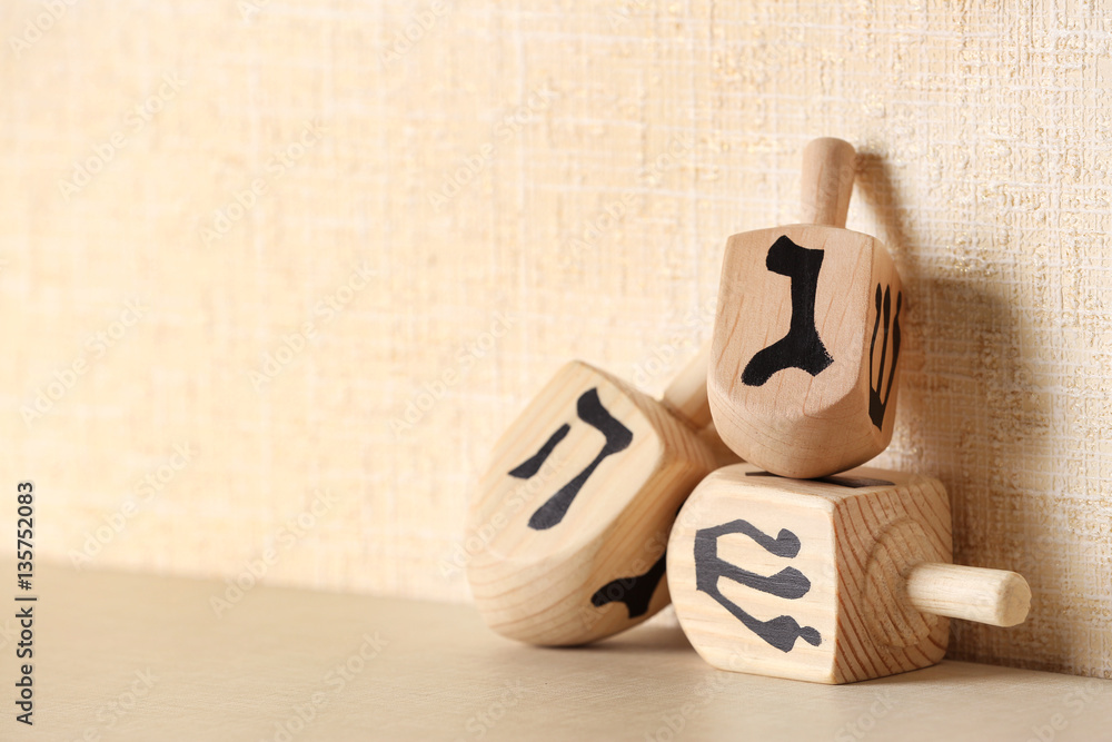 Dreidels for Hanukkah on light table against textured wall