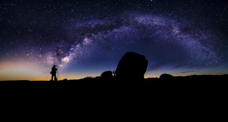 photographer doing astro photography in a desert nightscape with milky way galaxy. the background is
