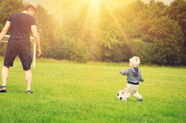 Wall Mural - Little boy playing football on the field with gates