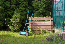 Manual Lawn Mower At A Wooden Compost Bin