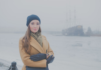 beautiful girl in winter on the waterfront against the backdrop of ancient ship