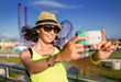 © EdNurg - Woman using smartphone to take selfie photo in amusement park at roller coaster background