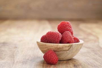 wood bowl full of ripe raspberries on old wooden table, with copy space