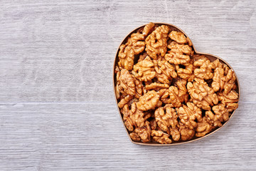 Heart-shaped box with walnuts. Peeled walnuts on wooden background. Healthy food for energy.