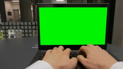 A POV shot of an office worker typing on a laptop with chroma key (green screen) included for compositing
