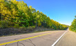 Summer highway open road to anywhere.
Sunny blue sky, woods on either side down a country highway in summer.  