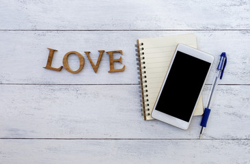 Wall Mural - Smartphone over notebook and wooden love text on wood texture background 