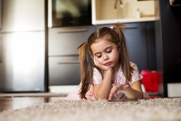 Bored little girl looking at tablet.