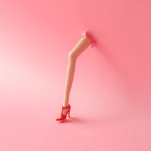 Doll Leg On High Heels Breaking Through Pastel Pink Wall. Creati