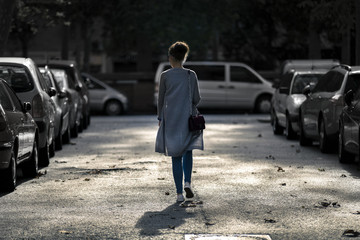 Young and slim woman in grey jacket is walking away along the st