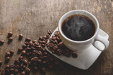 Fragrant hot coffee in a white cup with beans spilling roasted c