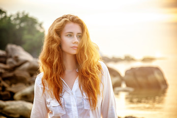 Wall Mural - Beautiful young woman with long red hair on the beach at sunset