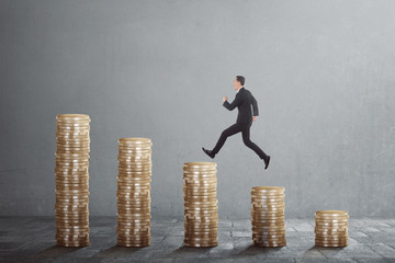 Happy asian businessman jump on between coin stacks